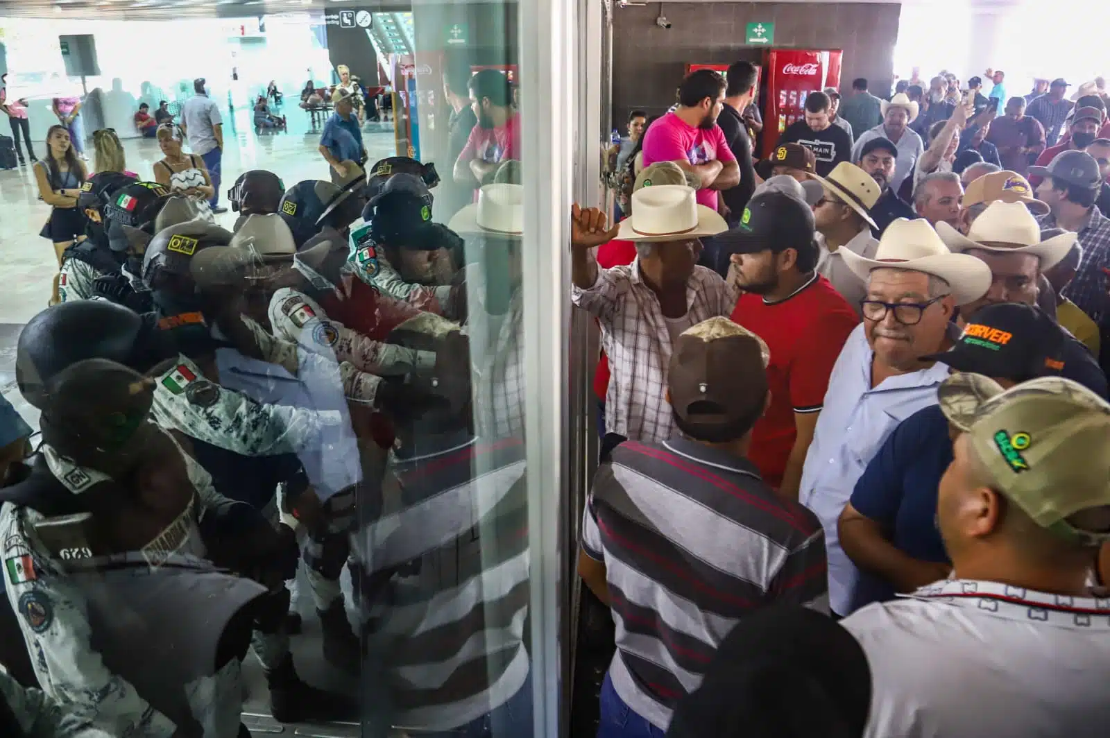 Agentes de la Guardia Nacional al interior del aeropuerto de Culiacán sosteniendo las puertas del otro lado productores agrícolas durante bloqueo y manifestación