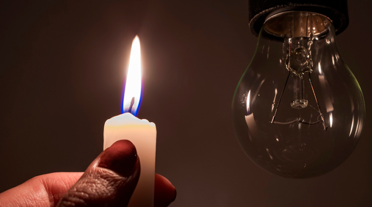 Una mano sosteniendo una vela encendida a un lado de un foco apagado