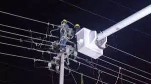 Dos personas arriba de un poste, un transformador y cables