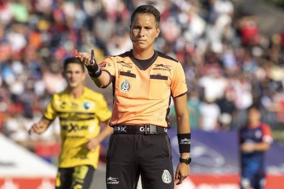 Una persona con un silbato en la mano y haciendo una seña, una persona atrás