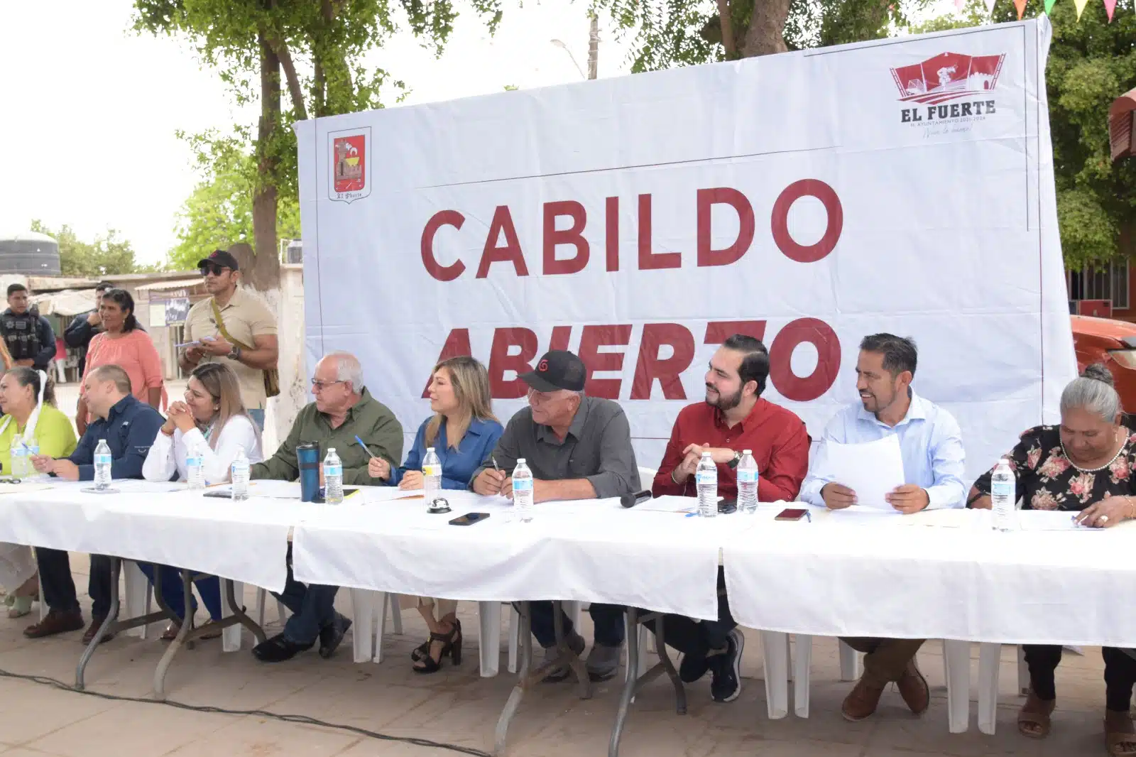 Funcionarios municipales y el alcalde de El Fuerte sentados en una mesa con mantel blanco y detrás de ellos el anuncio del programa conocido como Cabildo Abierto q