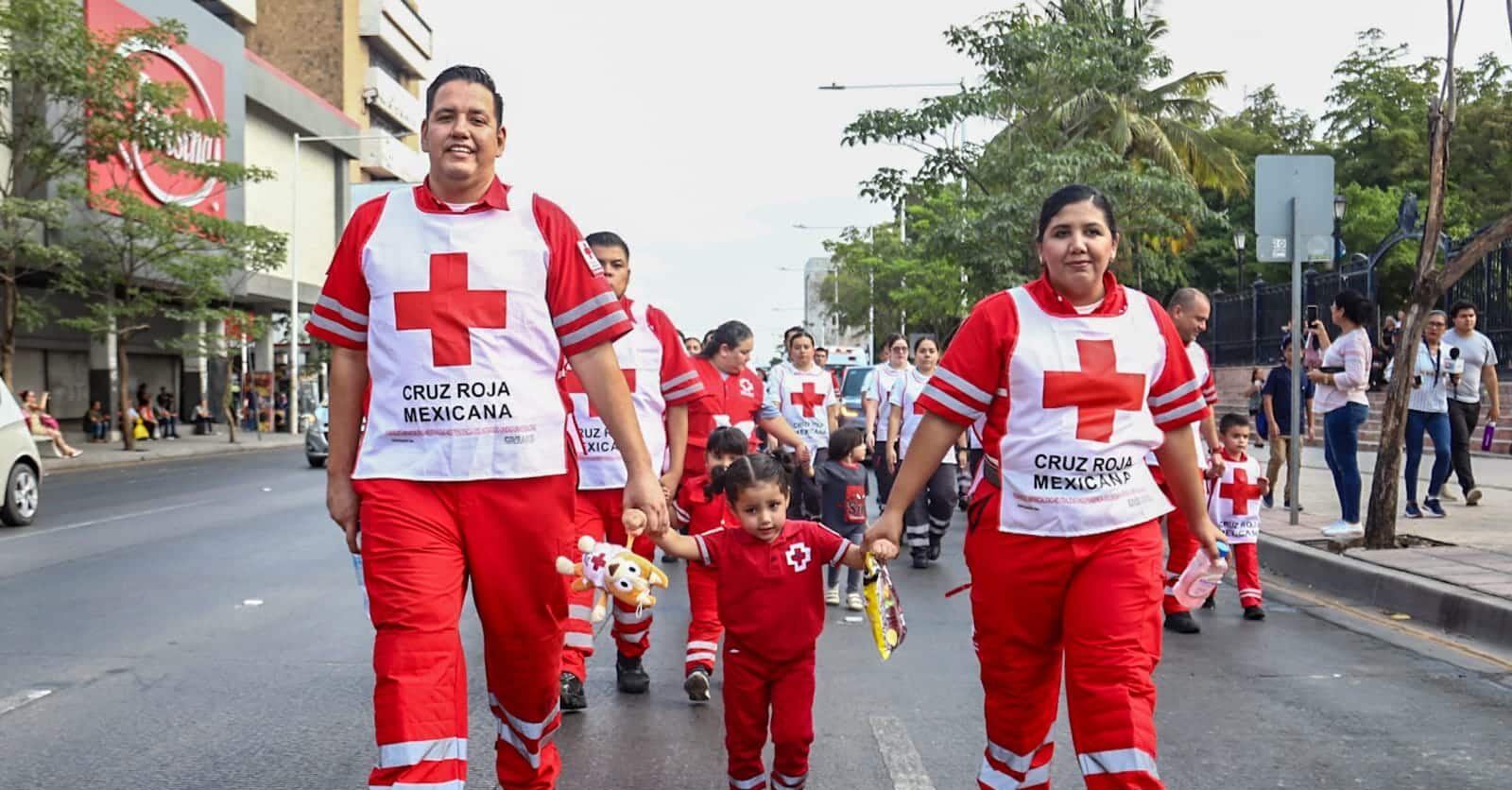 Niña tomada de las manos de sus padres en un desfile por el Día del Socorrista; ellos son voluntarios de Cruz Roja Culiacán