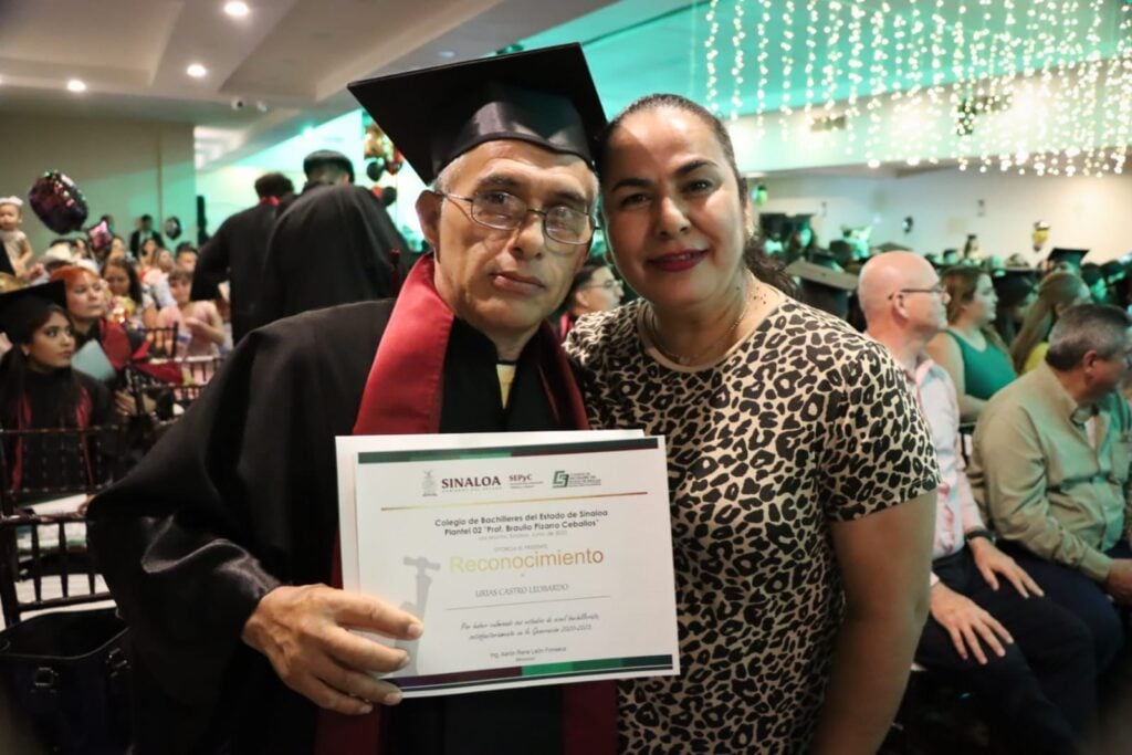 Un señor con toga, birrete y un diploma abrazado a una señora