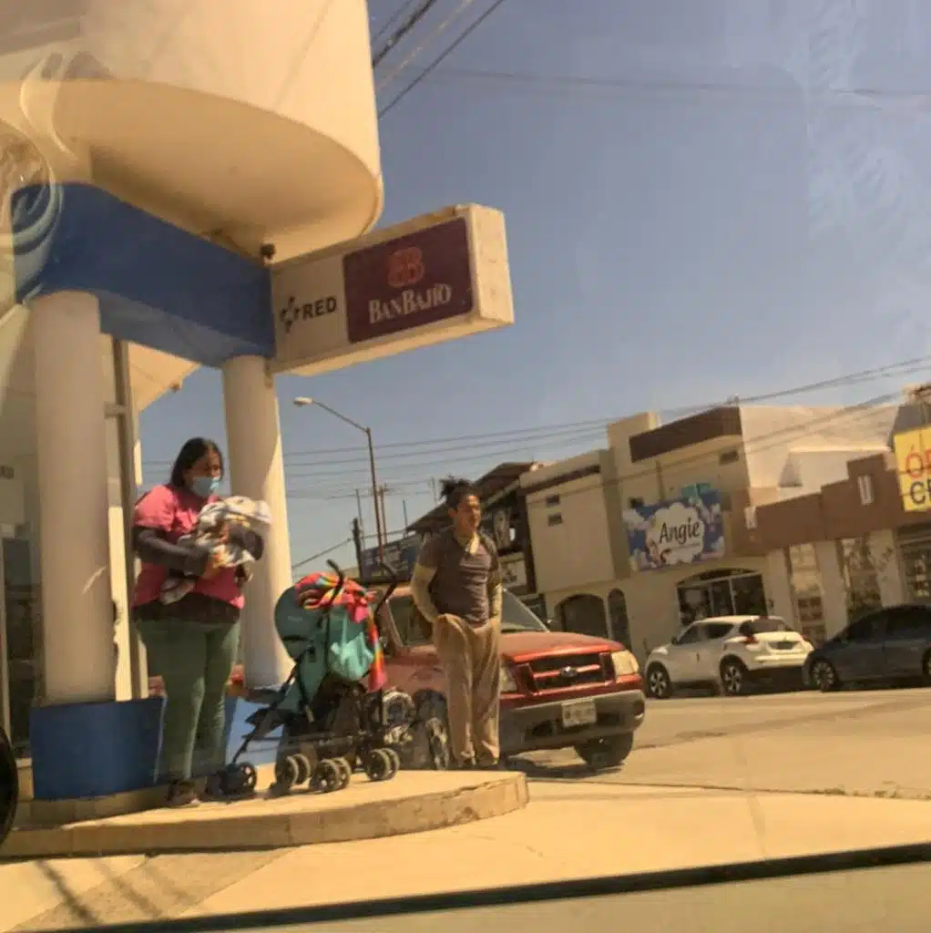 Dos adultos parados junto a una carriola y la señora sosteniendo a un bebé