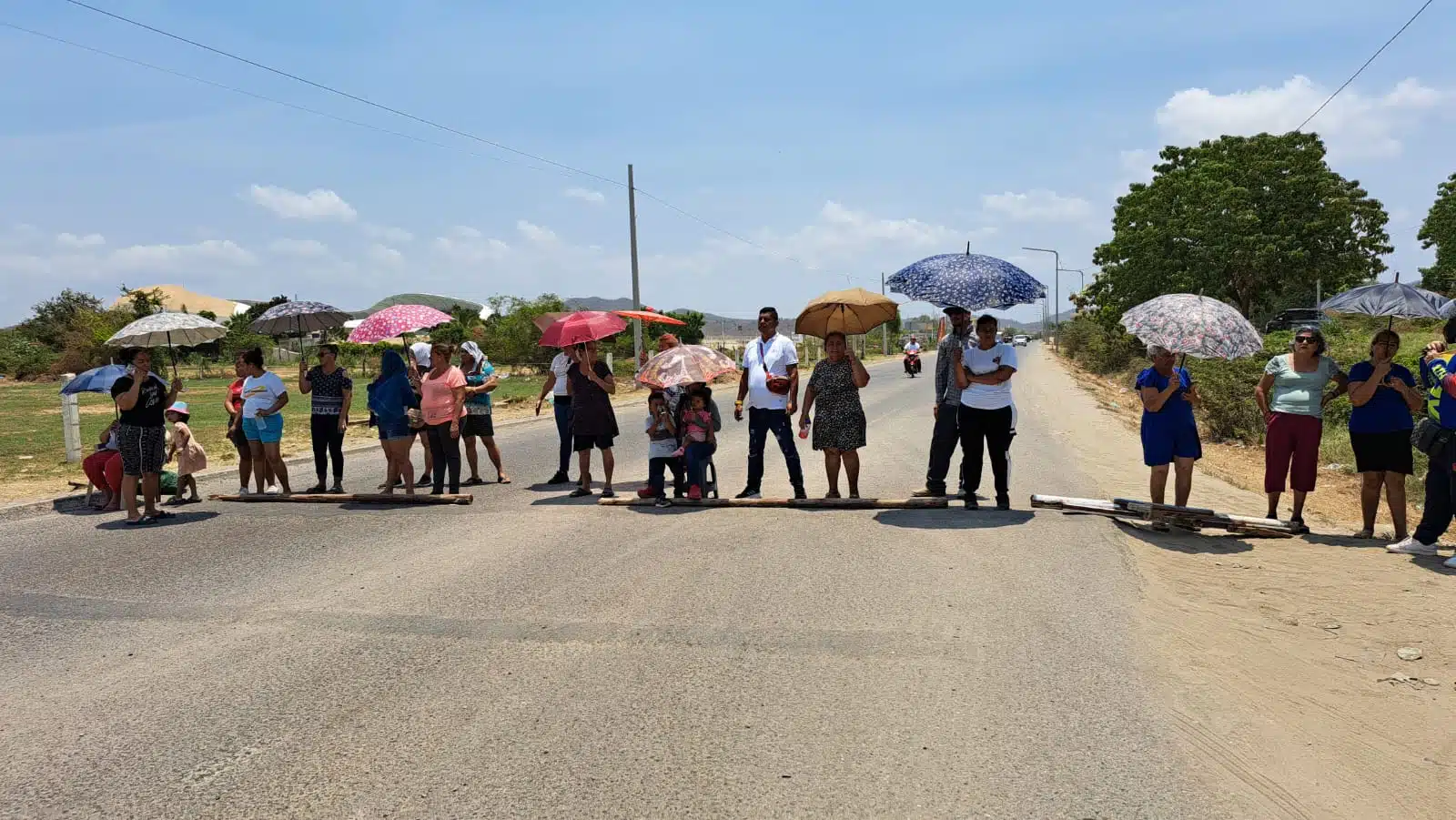 Bajo los rayos del sol habitantes de la colonia Líderes en Acción de Mazatlán se cubren con una sombrilla durante bloqueo de avenida Munich