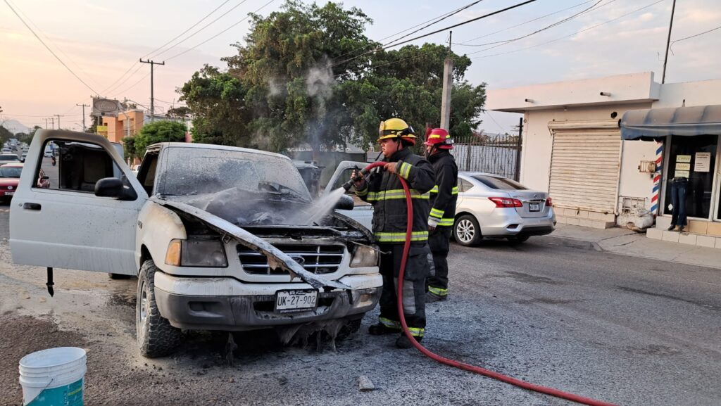 Bomberos de Culiacán utilizan una manguera para rociar agua en la parte delantera de una camioneta blanca Ford Ranger modelo 2001 que se Incendió tras un cortocircuito en el motor