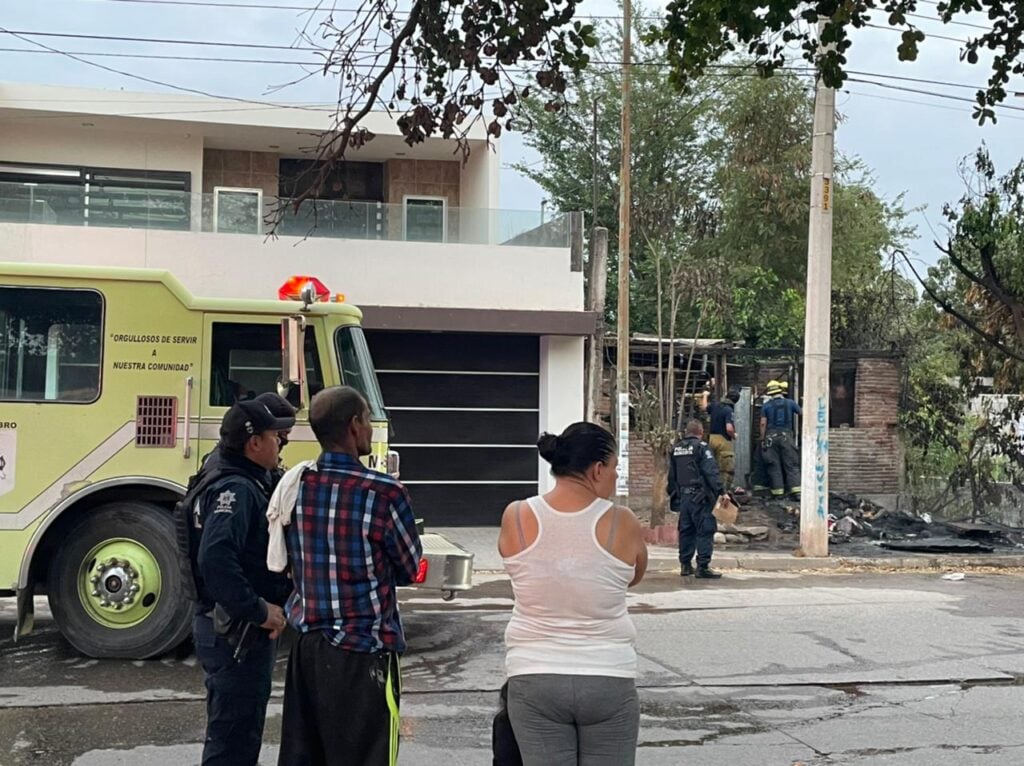 5 personas mirando hacia la casa quemada y un camión estacionado a un lado de otra casa