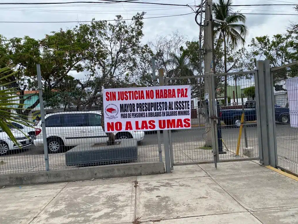 Lona pegada a una reja con una camioneta al fondo