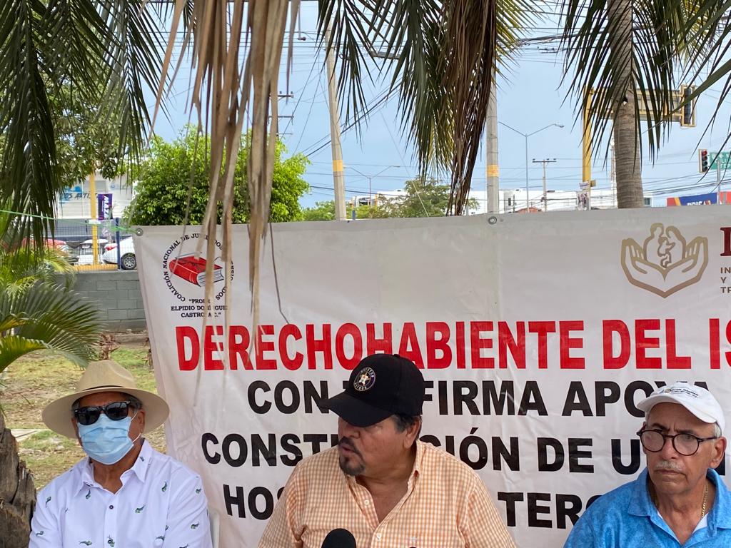 Tres señores sentados y atrás una lona
