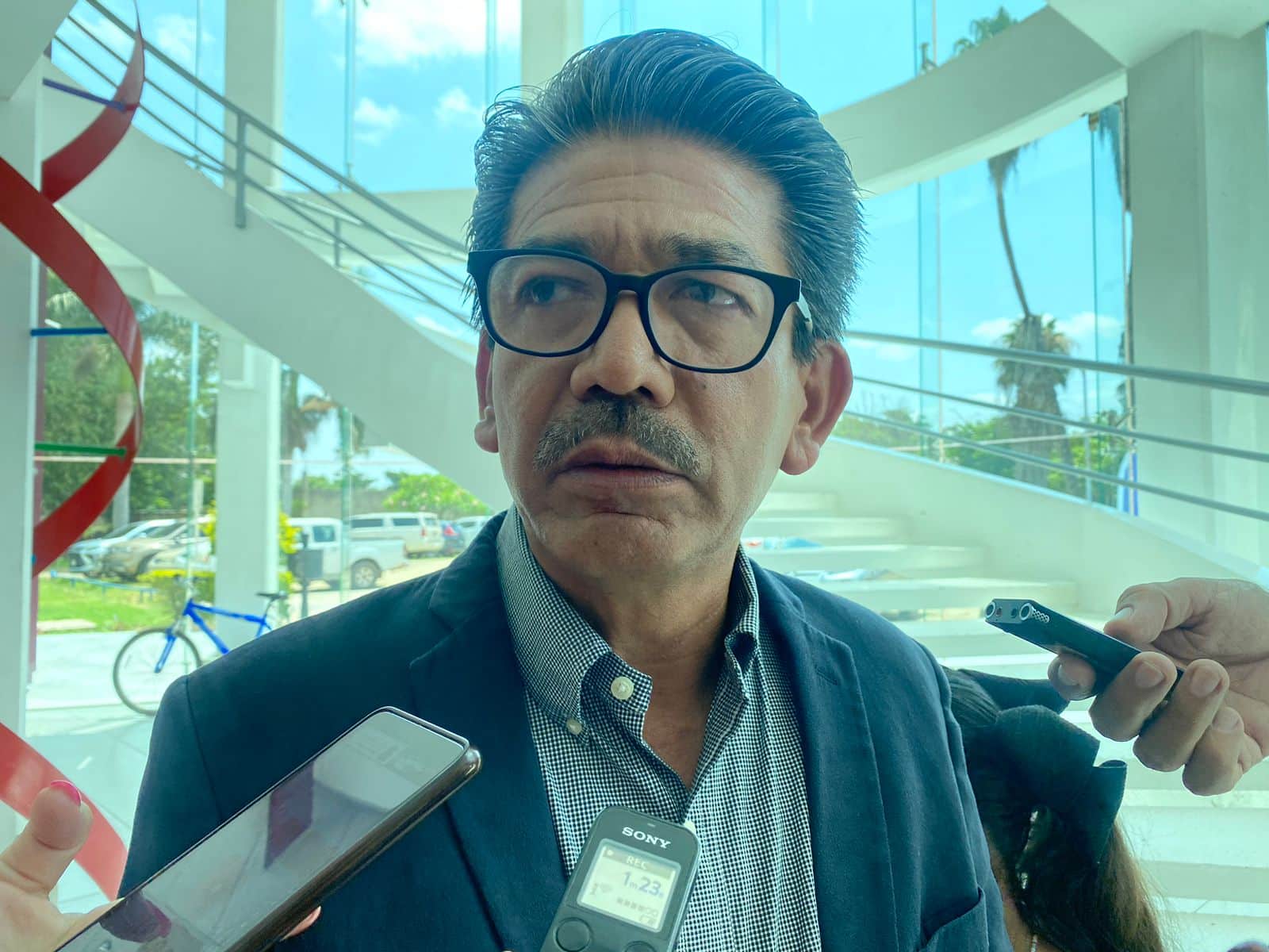 Martín Ahumada Quintero con lentes y en entrevista con los medios de comunicación, grabadoras y un teléfono celular