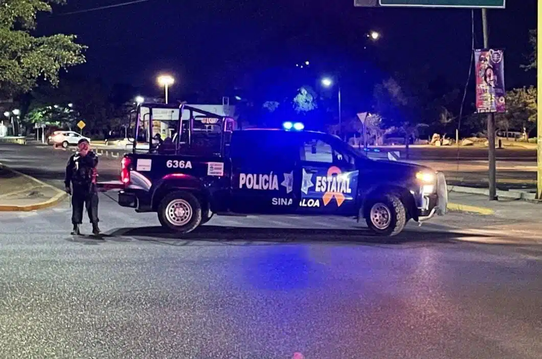 Camioneta de la Policía Estatal sobre una calle con un policía por un lado
