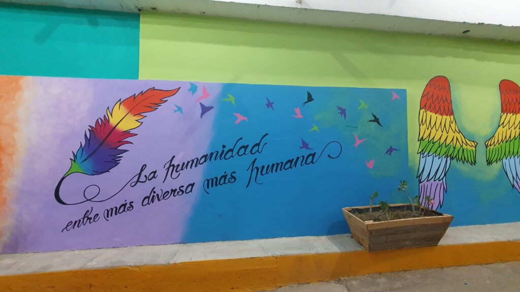 Frase escrita en la pared con colores de arcoíris de fondo y unas alas de ángel a la izquierda