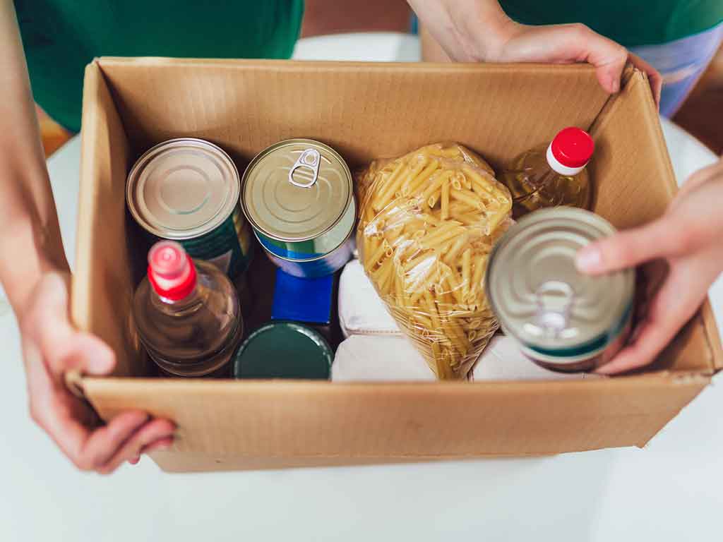 Manos sujetando una caja de cartón con despensa