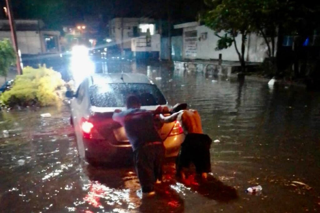 Civiles empujando su vehículo a través de una calle inundada