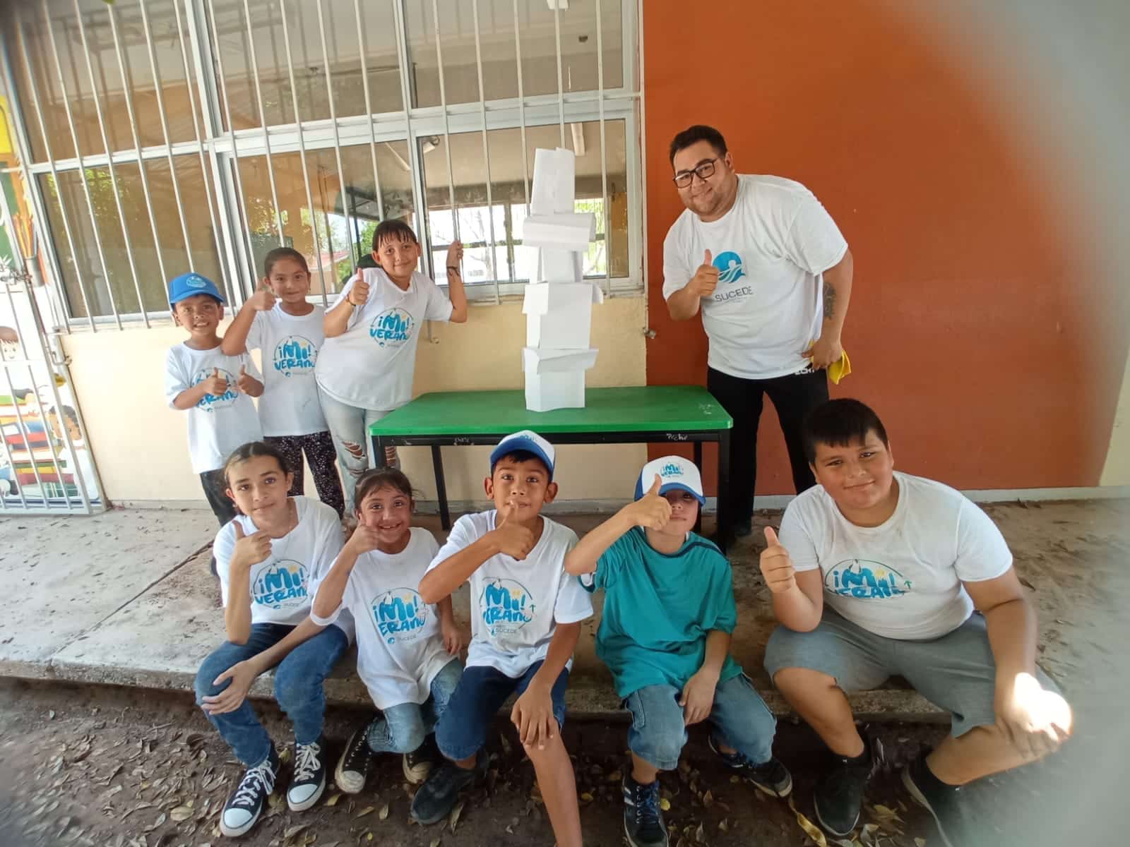 Pequeños y su auxiliar posando junto a su torre hecha con hojas de papel