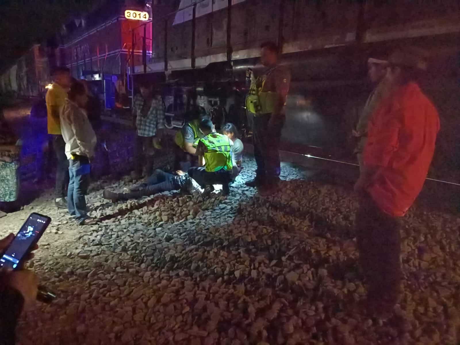 Tren parado sobre las vías, personas auxiliando a otra sobre unas piedras a un costado de la locomotora