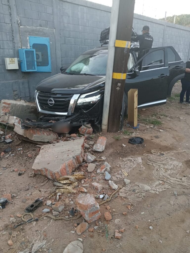 Camioneta negra chocada, poste, barda y piedras