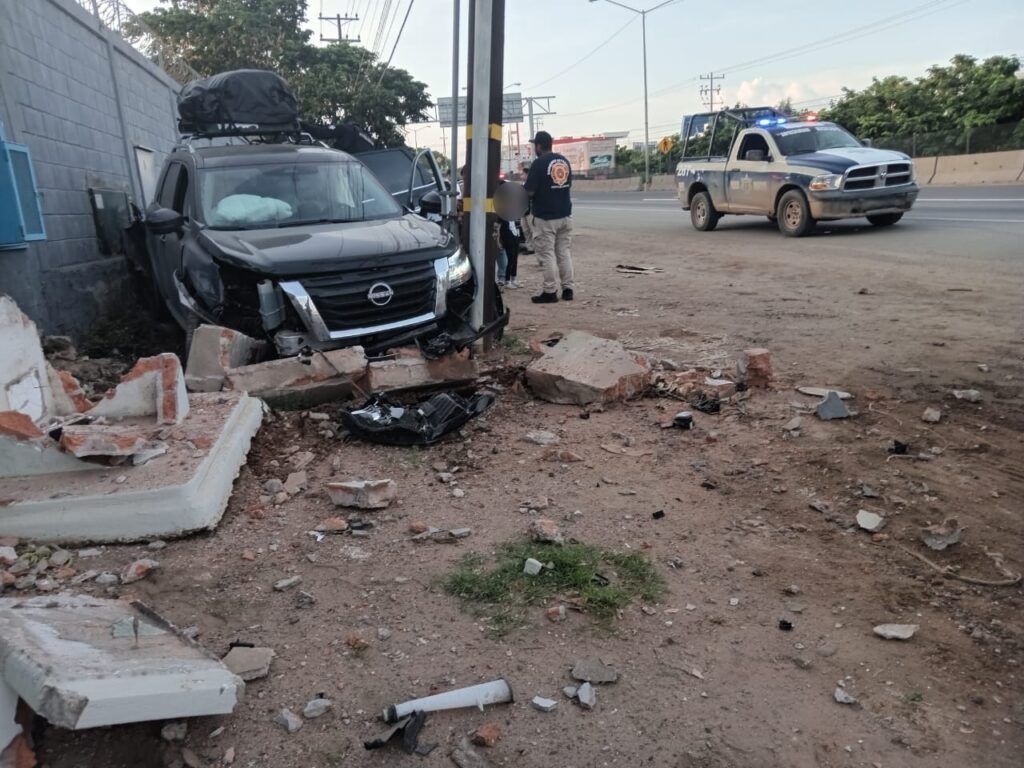 Camioneta negra chocada, poste, barda, piedras, una camioneta de la Policía Municipal y varias personas