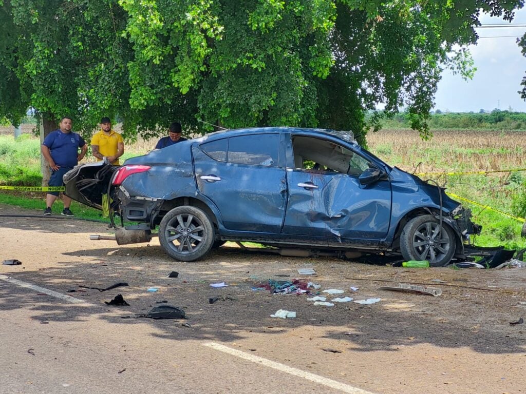 Un carro chocado, 3 personas mirando hacía él, árboles y parcelas