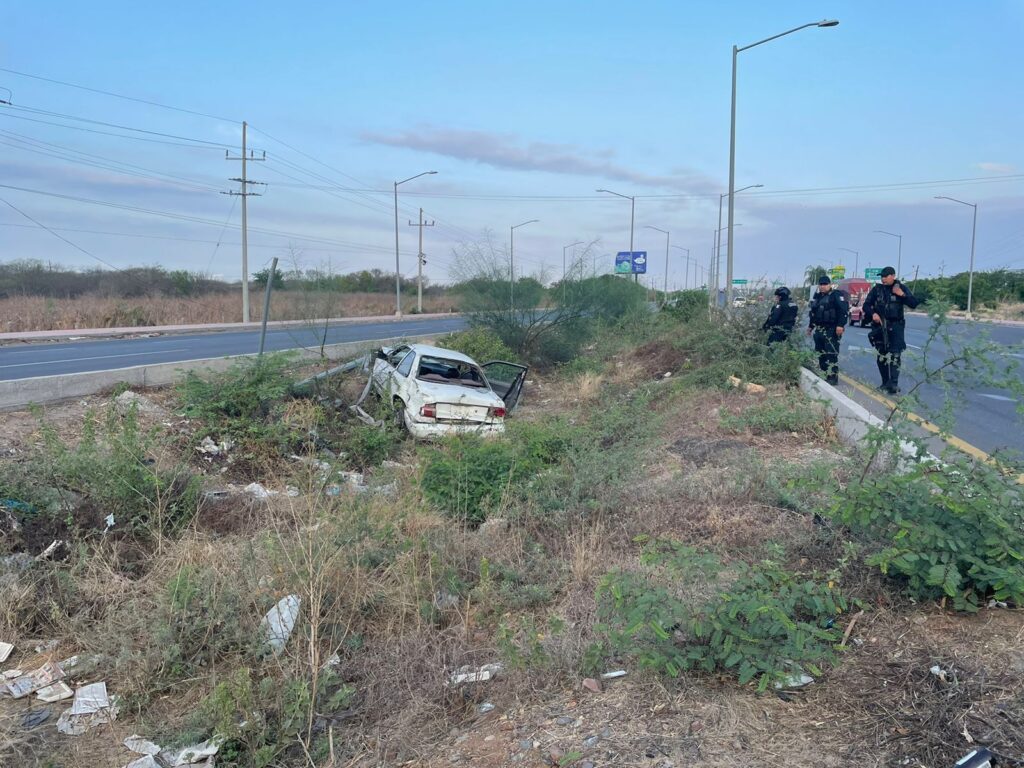 Un carro color blanco con la puerta del copiloto abierta y 3 personas mirándolo, postes de luz, carretera, arbustos, tierra y basura