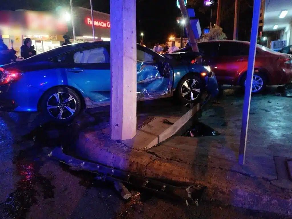 Un carro chocado con las bolsas de aire reventadas, un poste, banqueta y personas al fondo