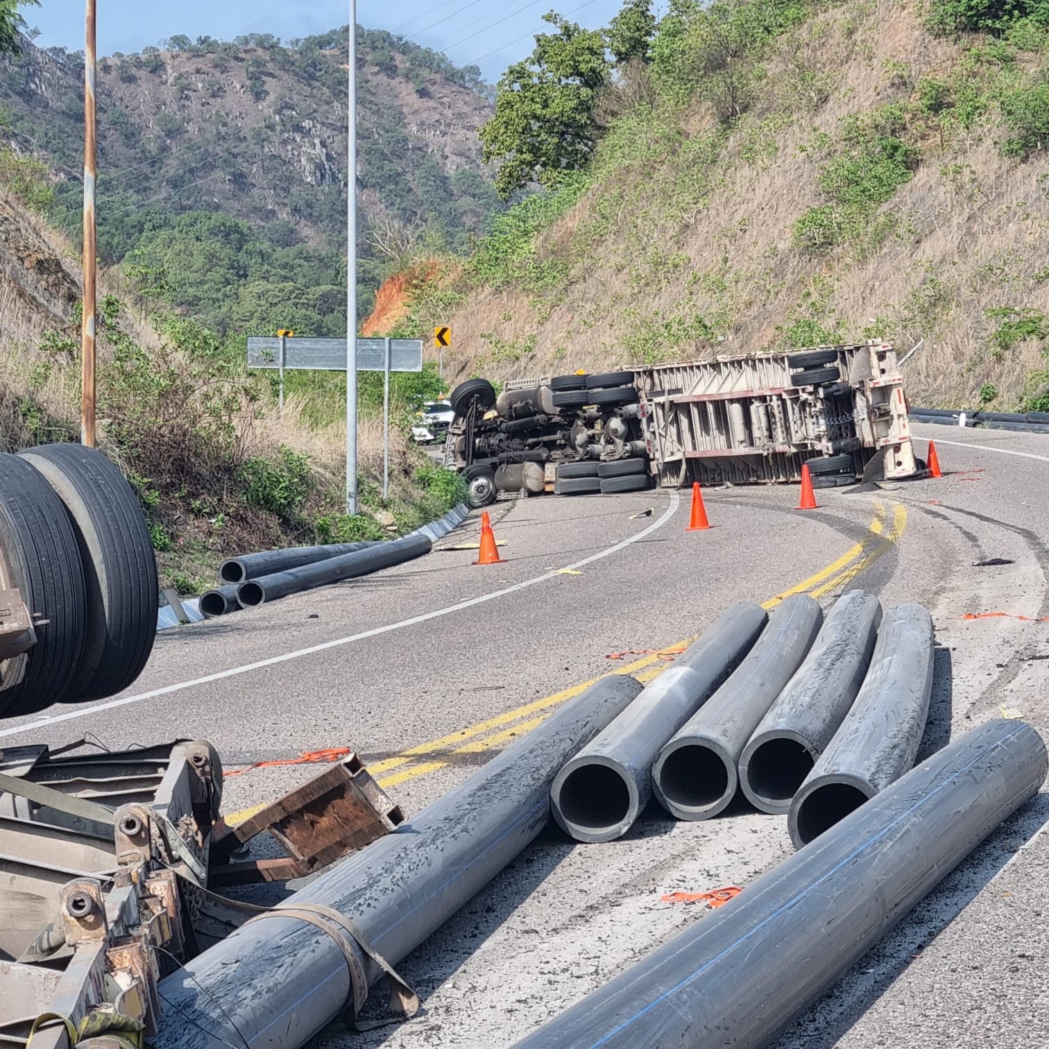 Tráiler volcado, tubos, carretera, cerros y árboles