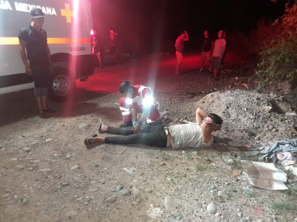 Una persona atendiendo. otra en el suelo, una ambulancia con las luces prendidas