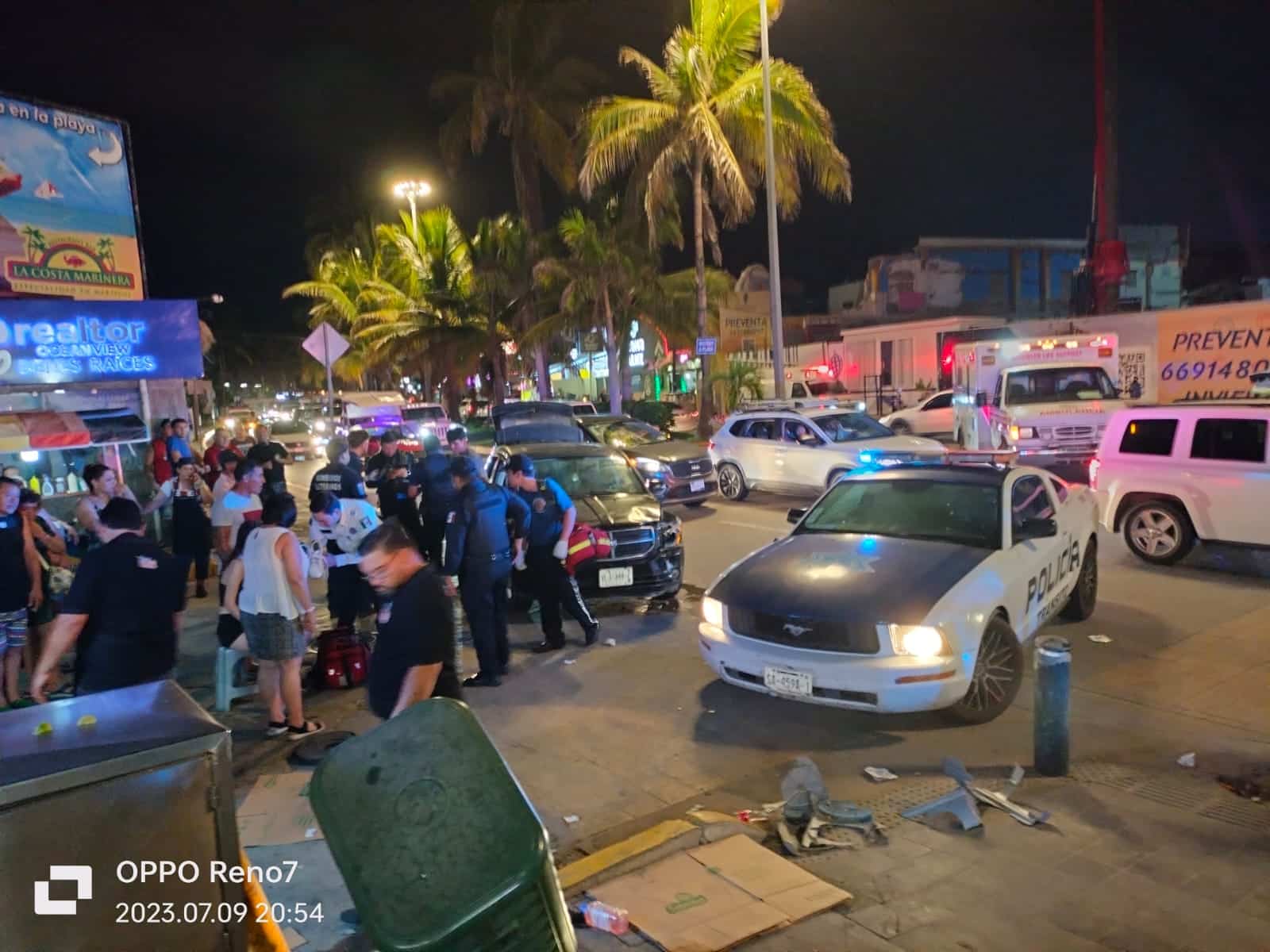 Personas paradas, un carro estacionado, una camioneta y varios carros al fondo