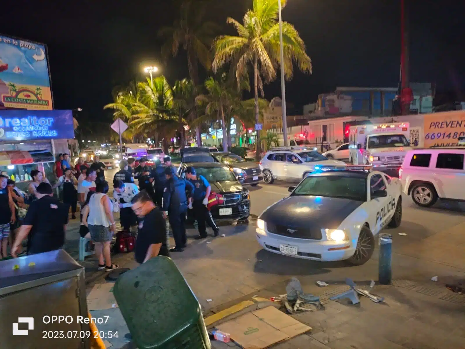 Personas paradas, un carro estacionado, una camioneta y varios carros al fondo