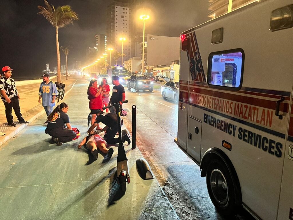 Ambulancia mujer tirada en la banqueta y gente socorriéndola tras caer de un patín del diablo