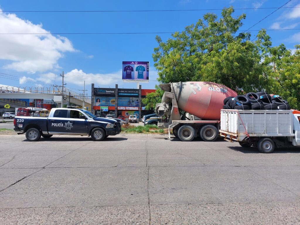 Un camión color anaranjado, una camioneta de policía y otra color blanca, carros, árboles, casas y negocios