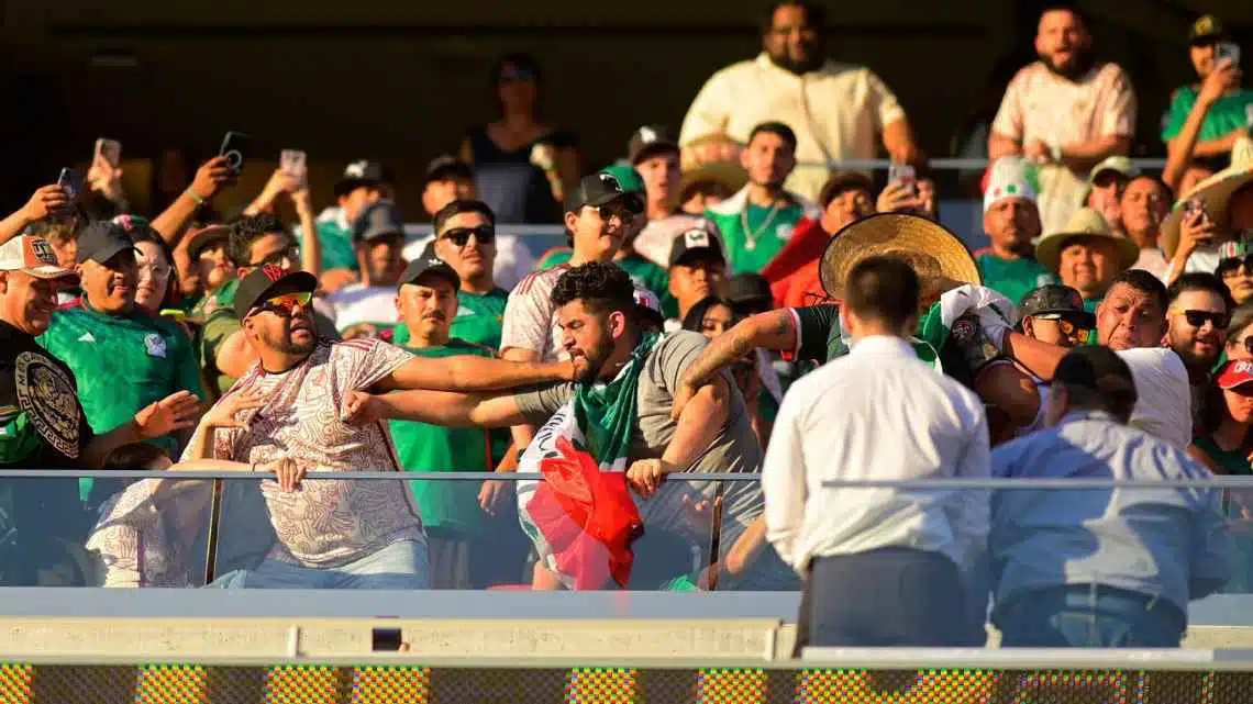 Muchas personas con playeras de ver y blanco del equipo de la Selección Mexicana parados en las gradas de un estadio de fútbol