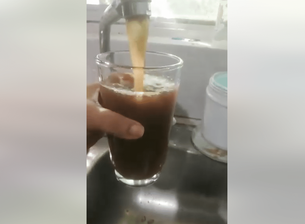 Llave de agua saliendo turbia, chocolatosa y con tierra, y un vaso de cristal