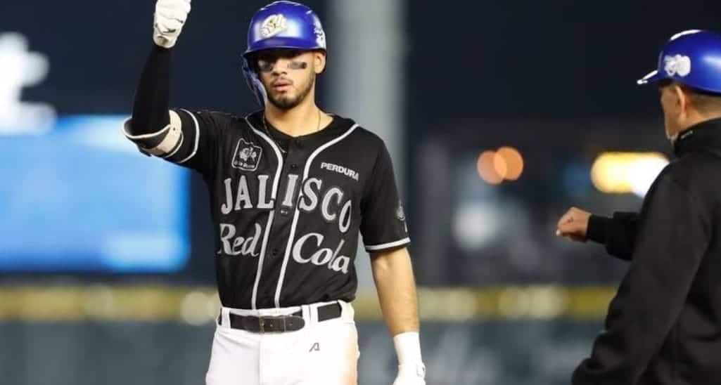 Una persona con un casco y uniforme de un equipo de beisbol con letras alzando la mano