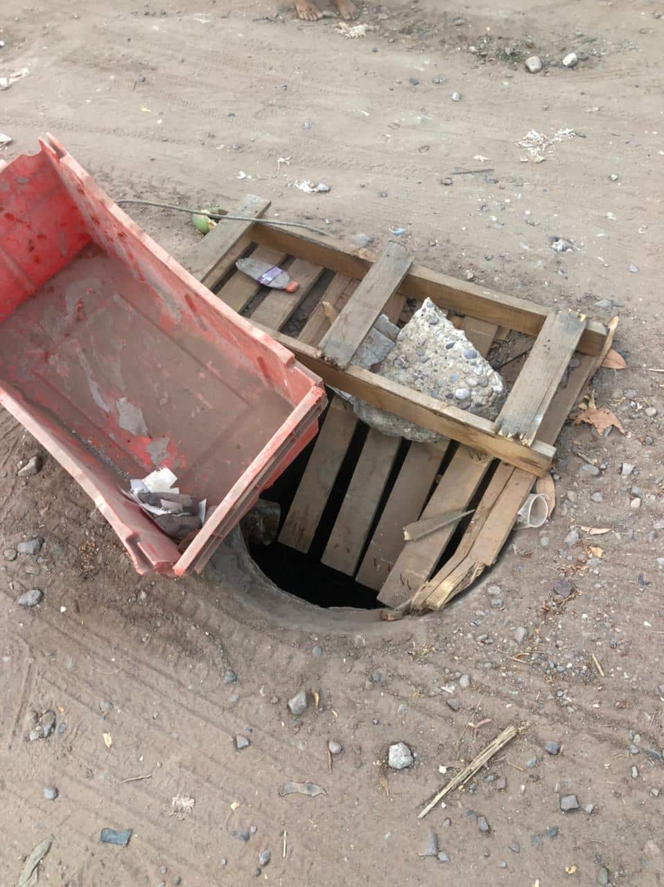 Una calle de tierra, una jaba y un pedazo de tabla tipo tarima tapando una coladera
