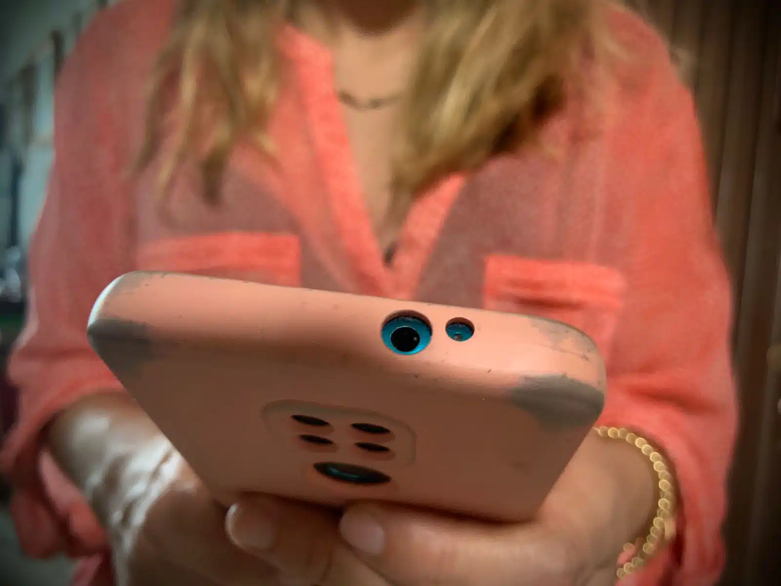 Una persona con blusa rosa y con un celular en la mano del mismo color