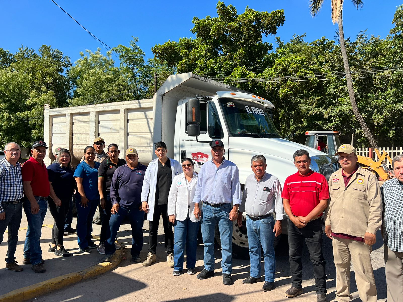 Muchas personas formadas para tomarse foto, árboles y un torton al fondo