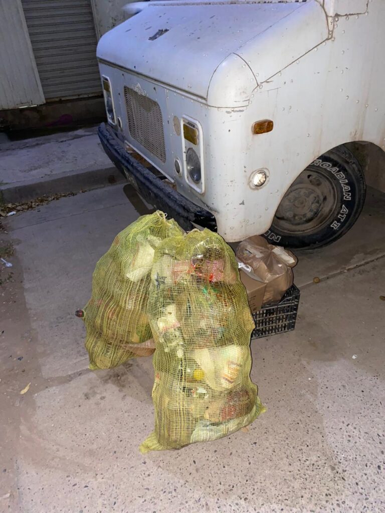 Bolsas de basura y una jaba sobre la calle, y la parte de frente de un camión estacionado