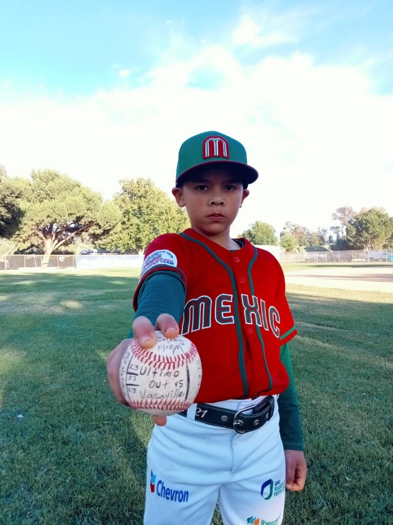 Un niño con gorra y una pelota de beisbol en una cancha con césped