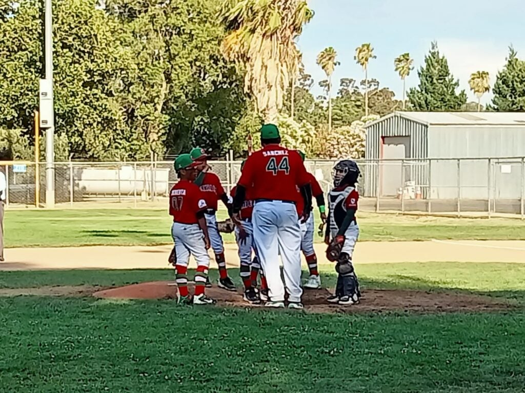 Niños y una persona adulta en la lomita de una cancha de beisbol