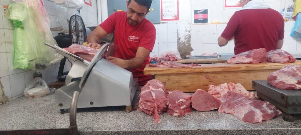 Dos personas, una de espaldas y la otra cortando con una máquina la carne, bolsas y carne en el mostrador