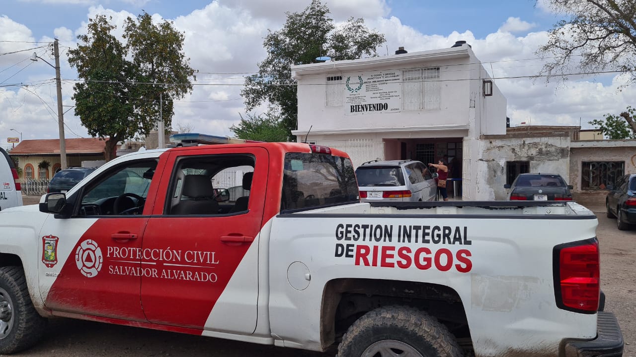 Una camioneta de la Protección Civil y al fondo una casa, árboles y el cielo con nubes