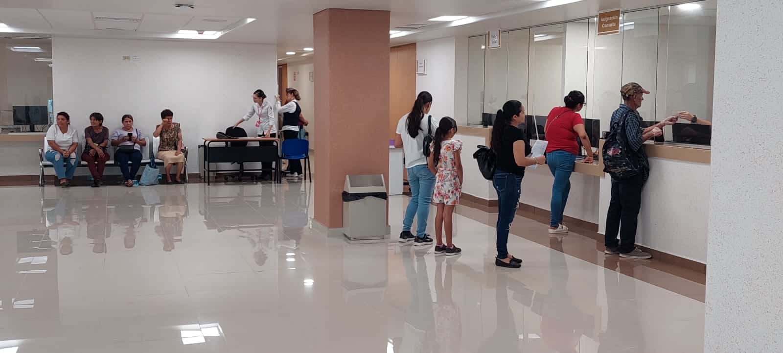 Personas sentadas y otras haciendo fila para ventanilla en un centro de salud