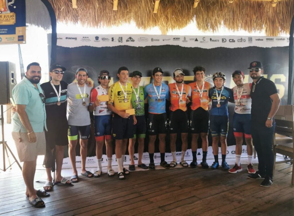 12 personas posando para una foto 10 de ellas con medalla colgada en el cuello, al fondo una lona