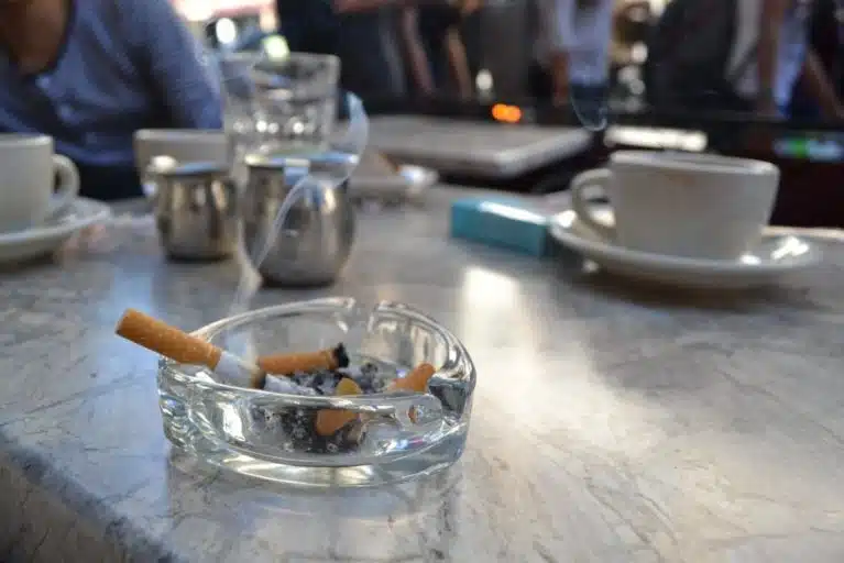 Cigarros en cenicero, mesa, tazas y brazos de personas