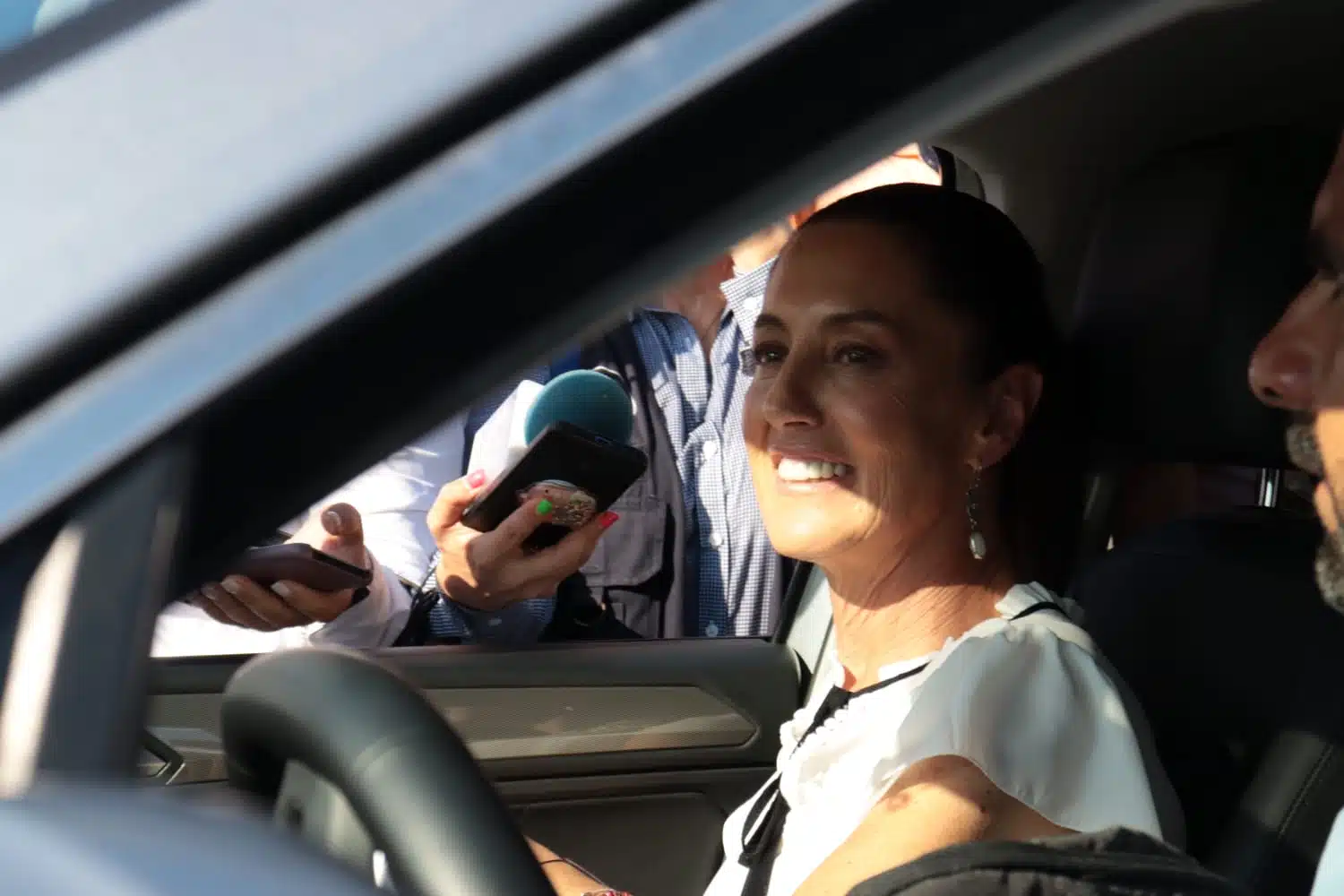 Una persona sonriendo arriba de un carro, micrófono de un medio de comunicación