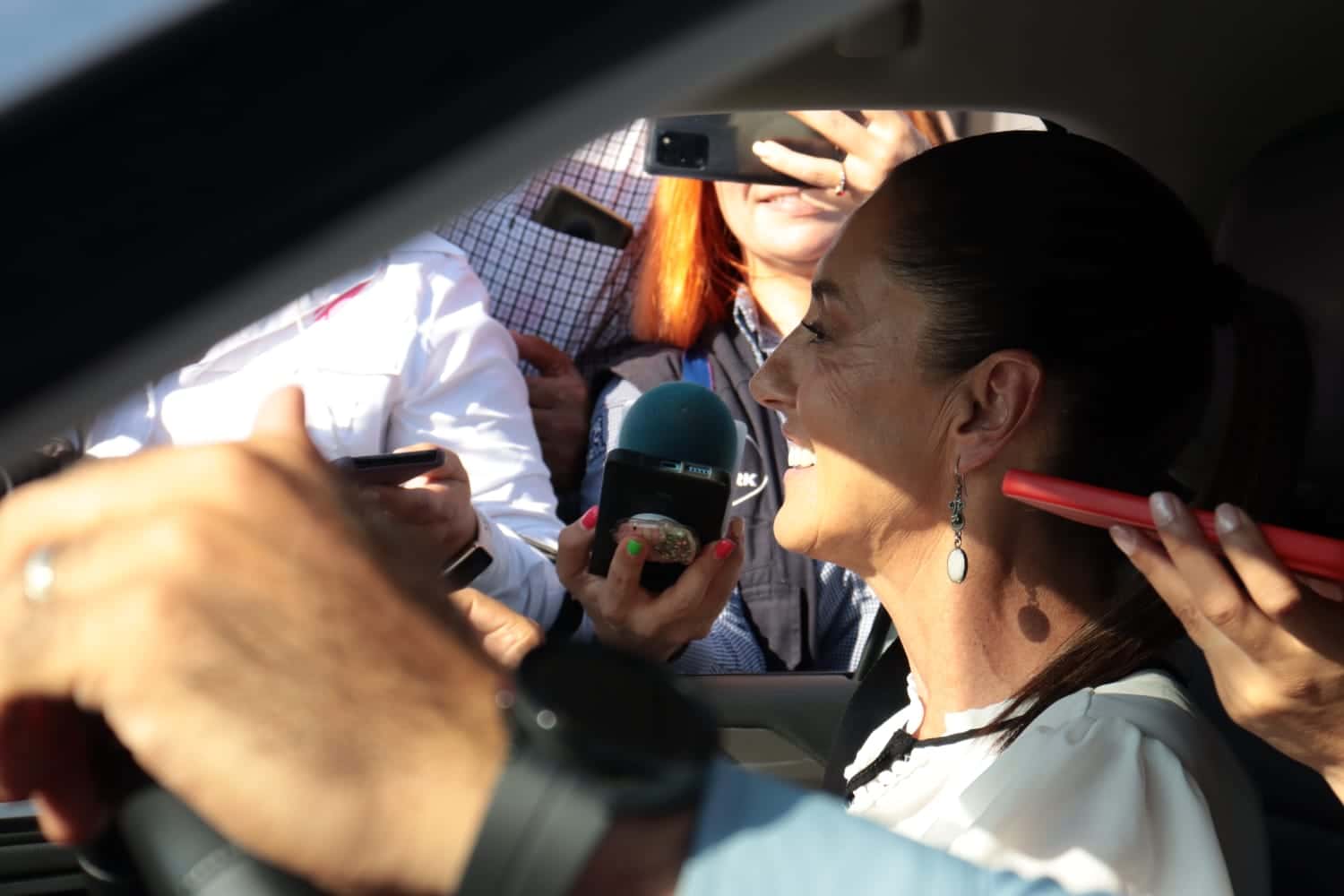 Una persona sonriendo arriba de un carro, micrófono de un medio de comunicación