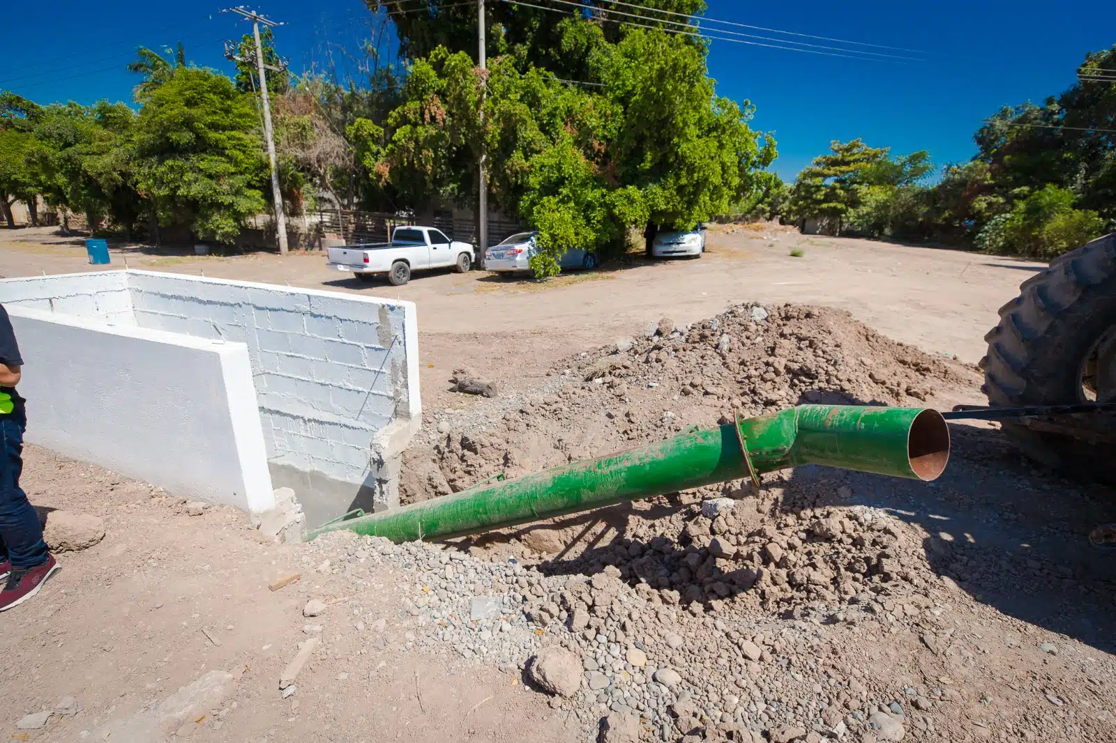 Paredes tipo barda de una estructura, 2 carros y una camioneta, la llanta de un tractor, postes, tubos, cables y árboles