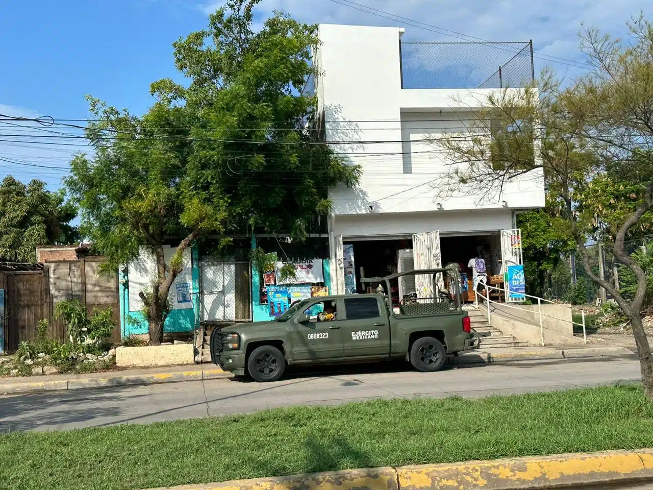 Una camioneta del Ejército Mexicano estacionada en una calle, una casa, césped y árboles