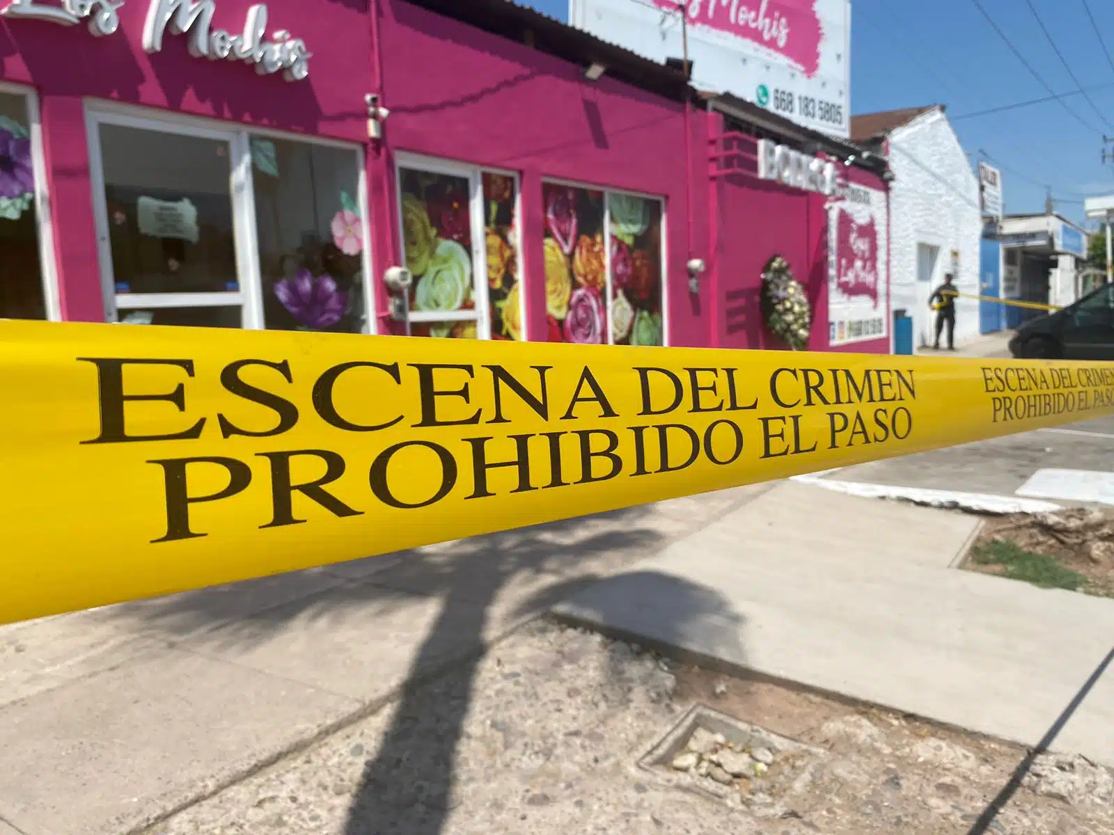 Cinta amarilla delimitando un área con letras Escena del crimen prohibido el paso, paredes de color rosa de un local de florería